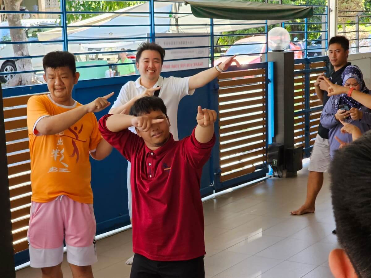 Two residents and a colleague copying a dance move together at PKKII Insan special needs home in Kuala Lumpur