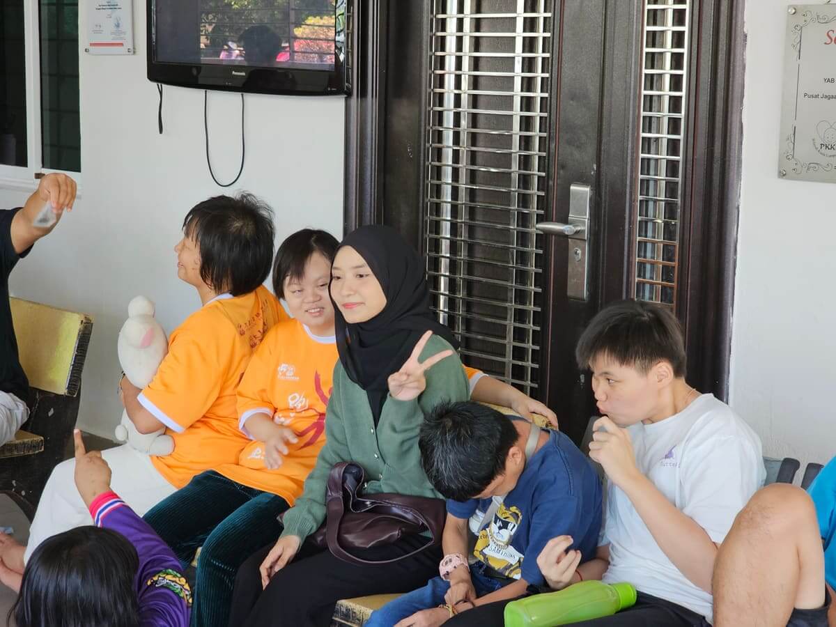 Residents and AGM Group volunteers circling red plastic chairs during a musical chairs game at PKKII Insan Home in Happy Garden, Kuala Lumpur
