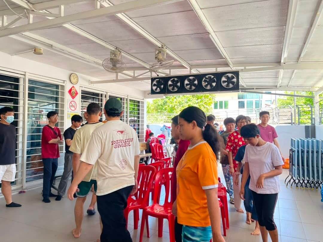 A volunteer sitting on a bench chatting with residents at PKKII Insan Home in Happy Garden, Kuala Lumpur