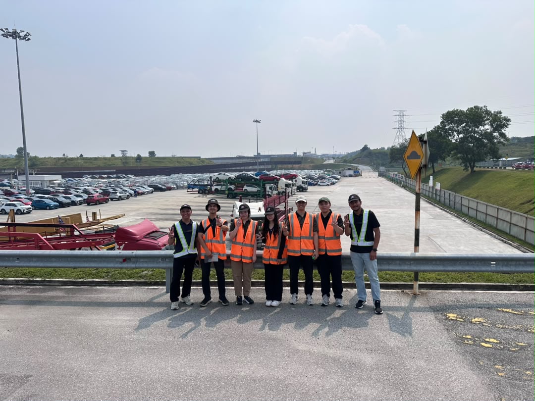 Advisory Apps team group photo in hi-vis vests at the Perodua Sungai Choh vehicle stockyard on 24 August 2026, with rows of finished vehicles and car carriers behind them